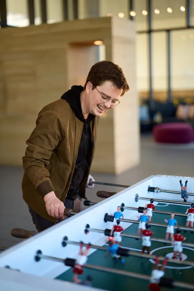 Man with glasses laughing while playing foosball indoors, a fun personality dating profile photo in Austin